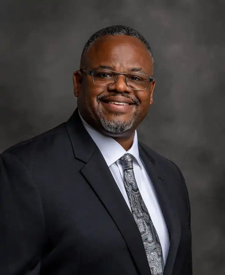 Smiling middle-aged African American man wearing glasses, a suit, and tie in a professional portrait.