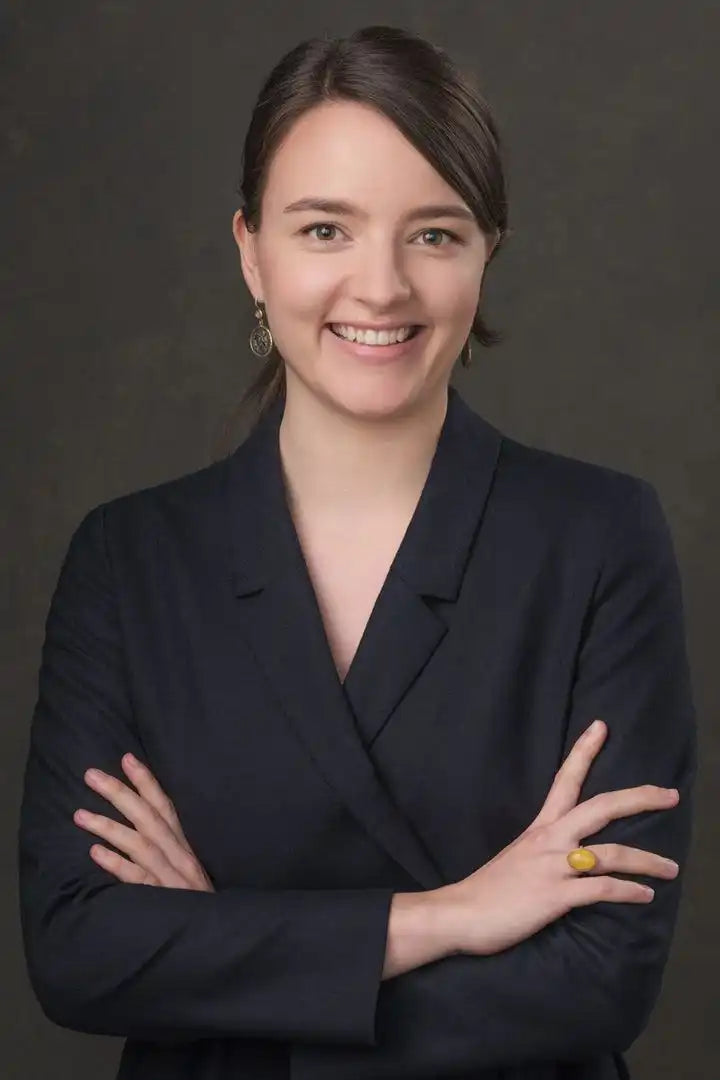 Smiling woman in a dark blazer with arms crossed.