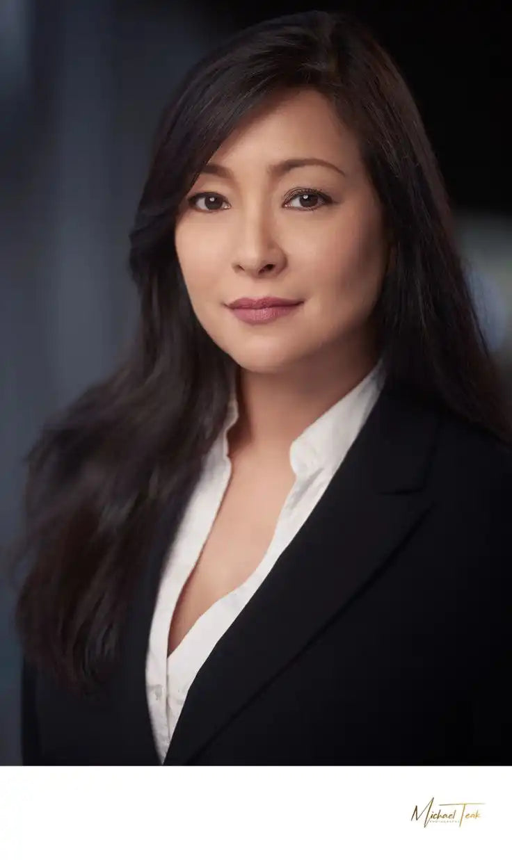 Woman with long dark hair wearing a white blouse against a dark background.