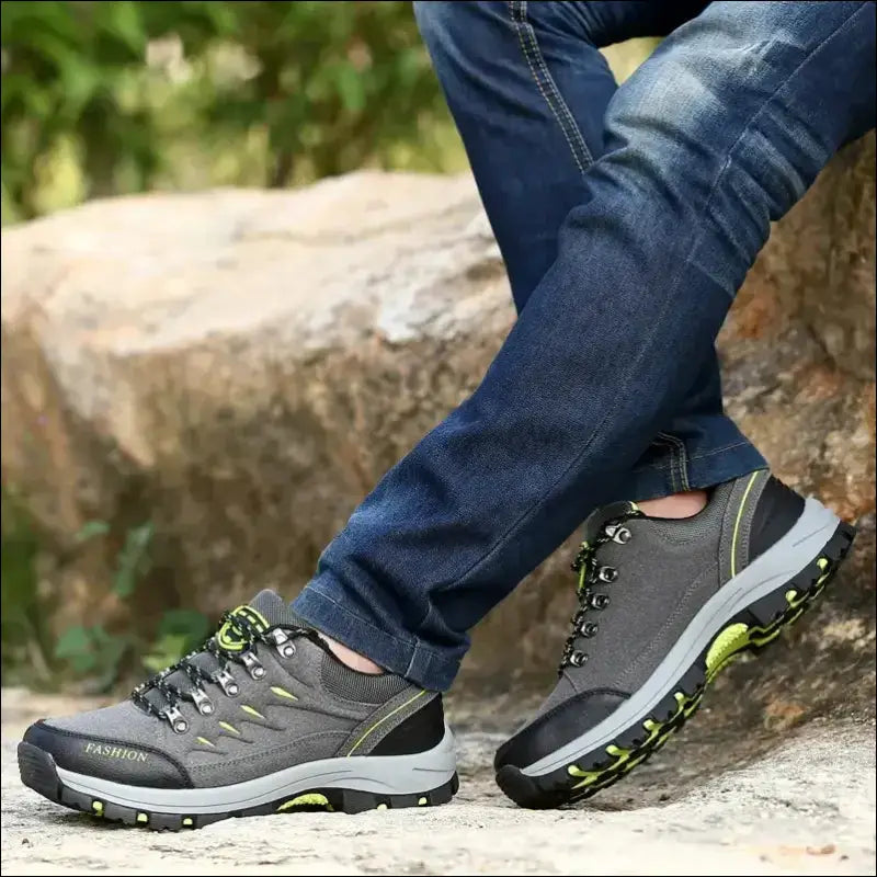 Pair of gray hiking shoes with green accents worn on feet in jeans.