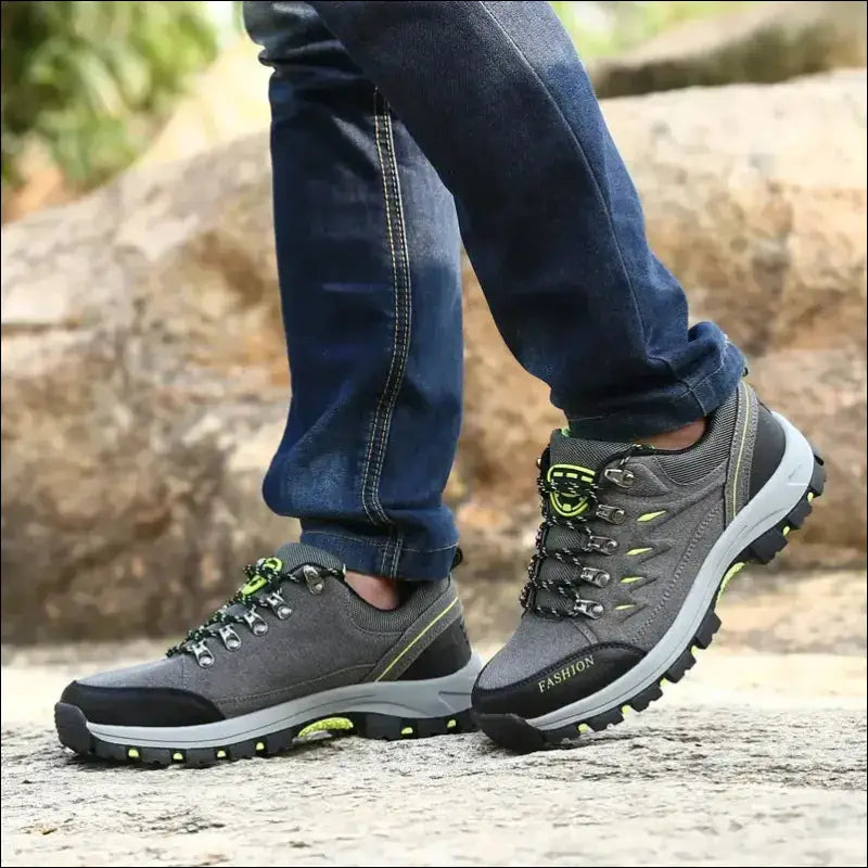 Pair of gray hiking shoes with green accents worn on feet in jeans.